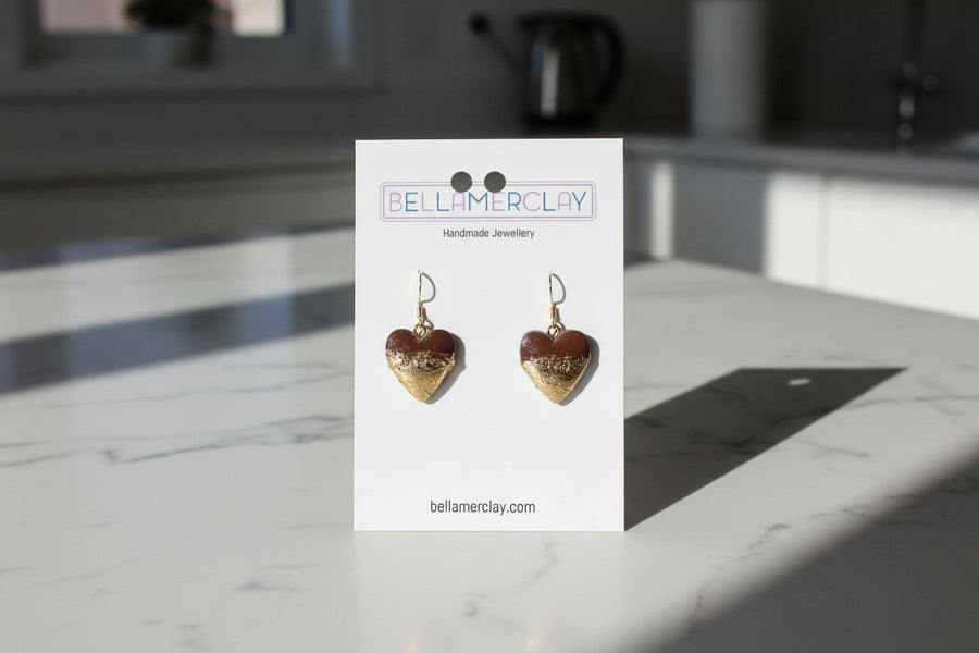 Heart-shaped gold earrings on a Bellamerclay branded card against a neutral background